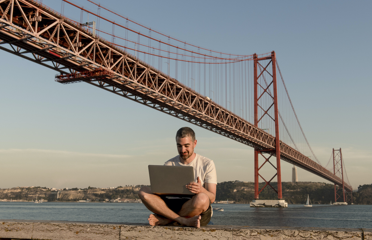 Man using laptop at 25th of April Bridge in Lisbon, Portugal